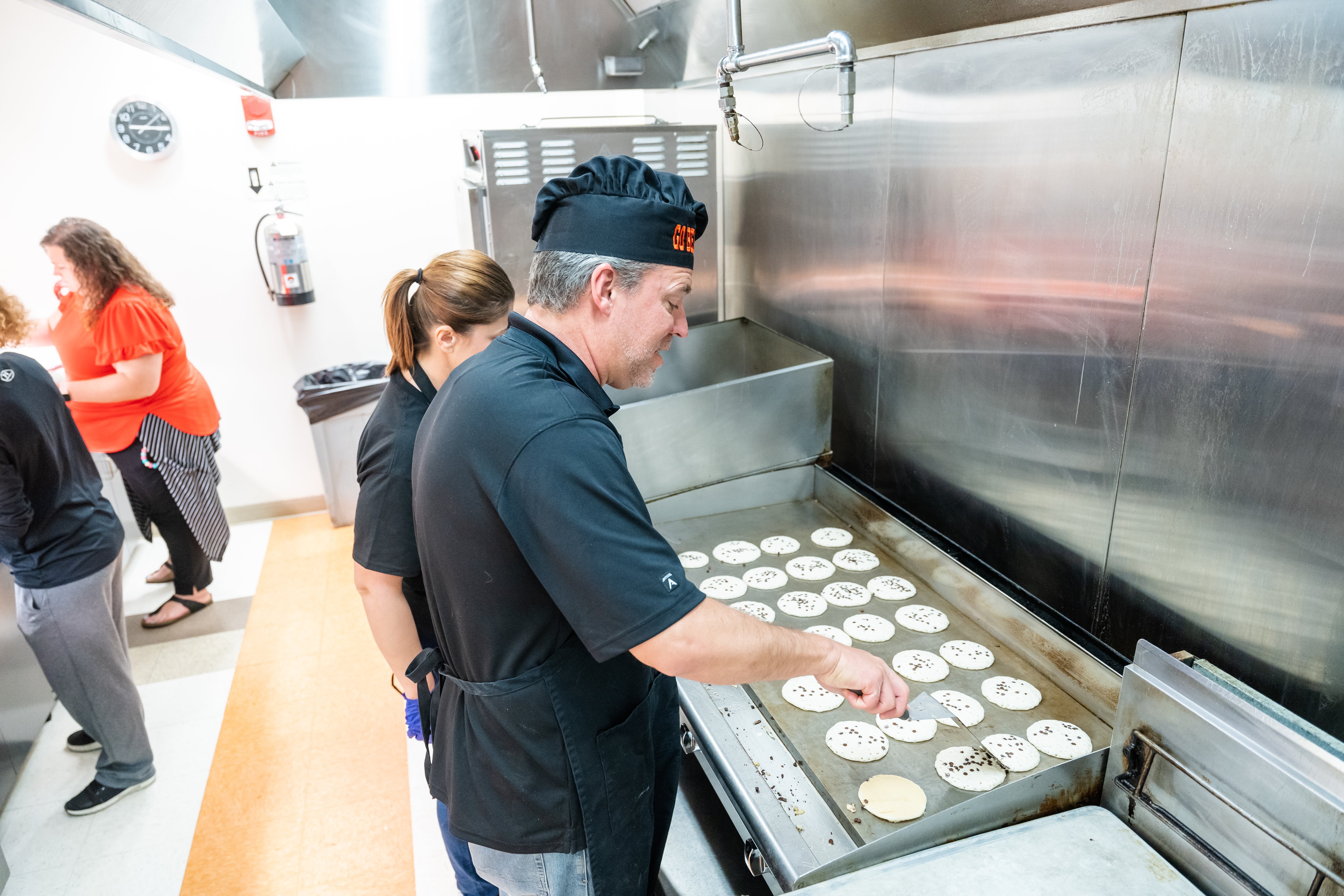 Dr. Webb cooks at Pancake Breakfast in chef's hat in large kitchen