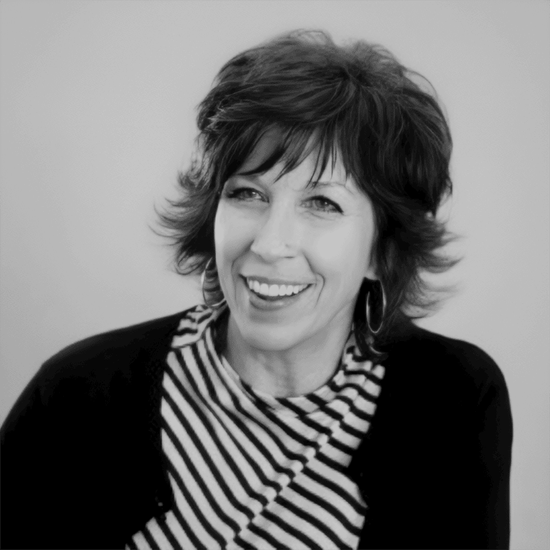 Woman with short, wavy hair smiling, wearing hoop earrings and a striped top with a dark cardigan.